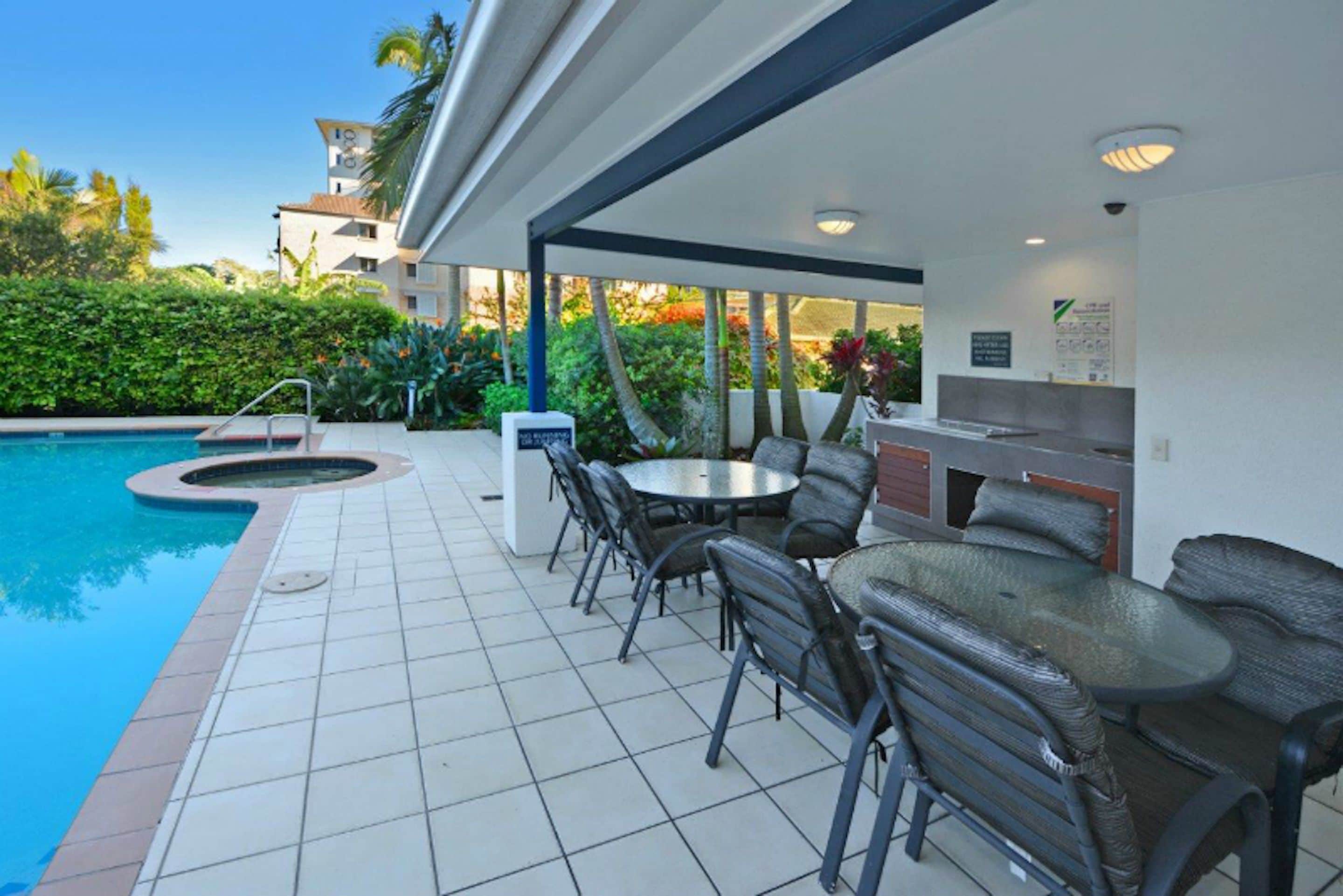 Zona de piscina exterior con jacuzzi, mobiliario y una parrilla.