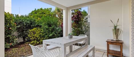 A patio with a white table and chairs, a wooden bench, and a small plant on a side table.