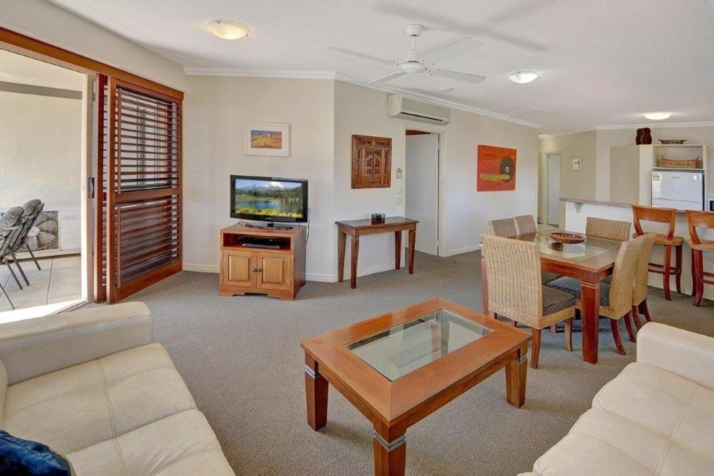 A living room with a television, wooden furniture, and a dining area with chairs and a table.
