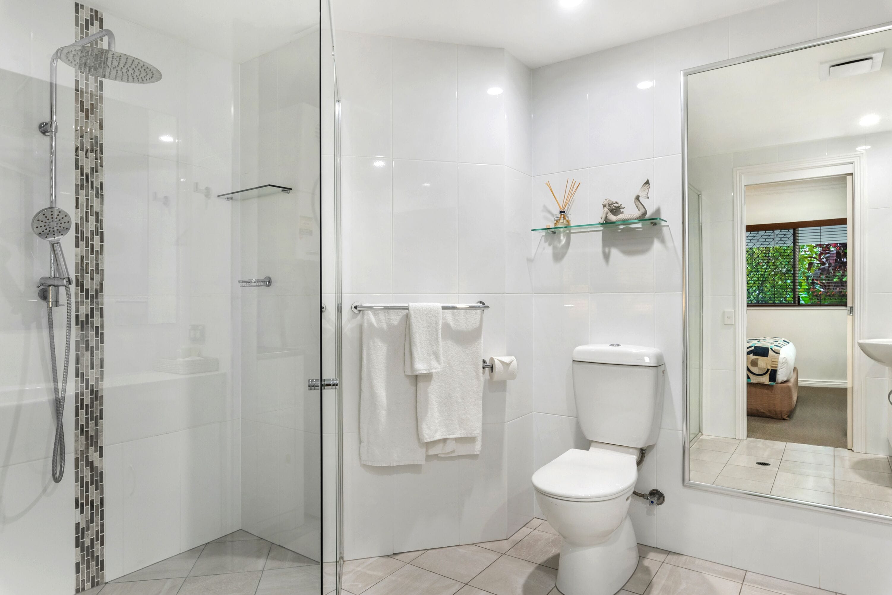 Ein modernes Badezimmer mit einer Duschkabine, einer Toilette und einer Glasablage mit Dekoration.