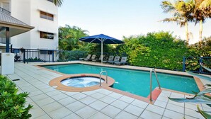 A swimming pool with a hot tub, lounge chairs, and an umbrella.