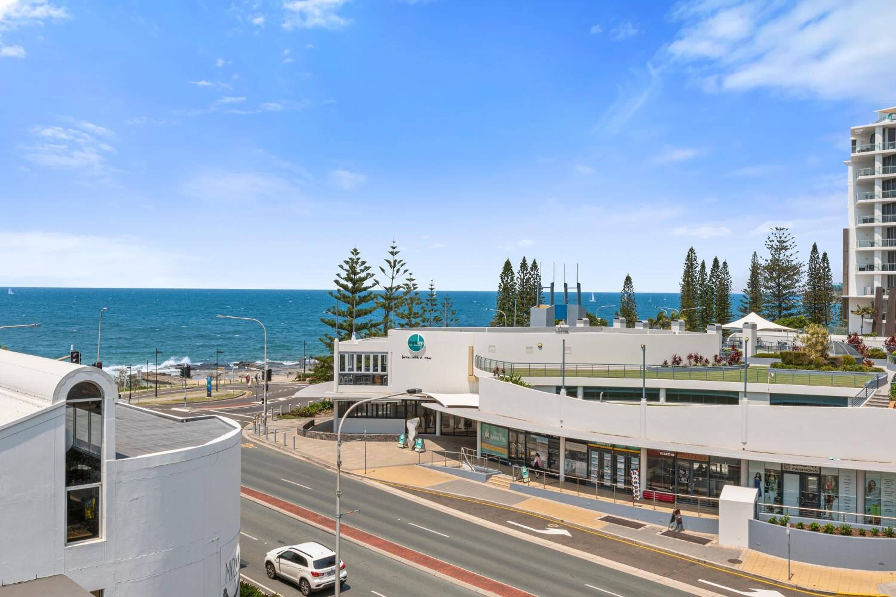 A coastal building with a curved facade, a pedestrian walkway, and a view of the ocean.