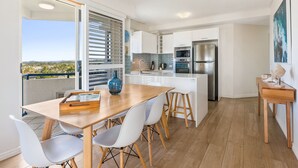 A modern kitchen with white cabinets, a stainless steel refrigerator, and a wooden dining table with white chairs. - Raffles Mooloolaba (Mooloolaba)