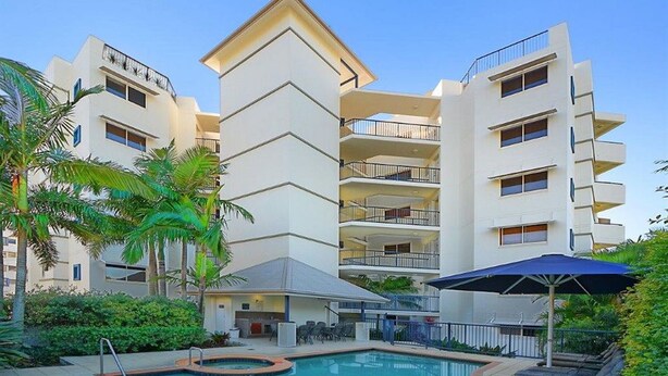 A modern hotel with a pool area, outdoor seating, and multiple balconies.