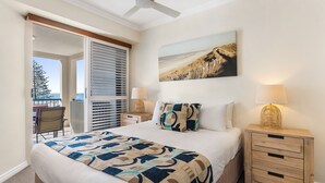 A bedroom with a bed, a nightstand, a lamp, a painting, and a view of the outdoors. - Raffles Mooloolaba (Mooloolaba)