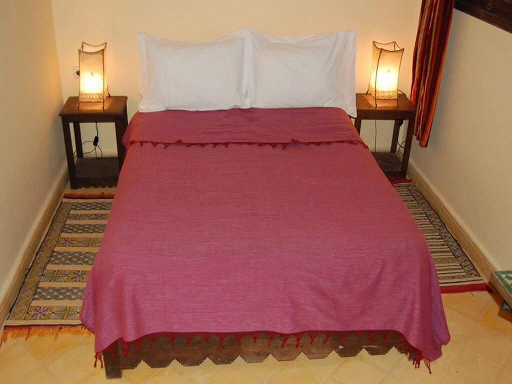 Un lit avec une couvre-lit rouge, des oreillers blancs et deux lampes de chevet.