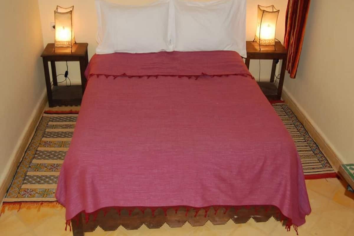 A bed with a red bedspread, white pillows, and two bedside lamps.