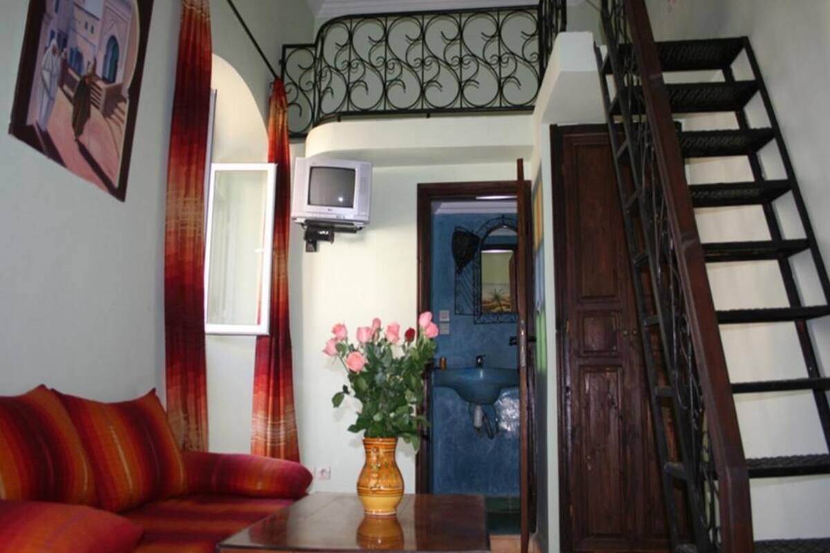 Uma sala de estar com sofá, mesa, vaso com flores, televisão e escada.