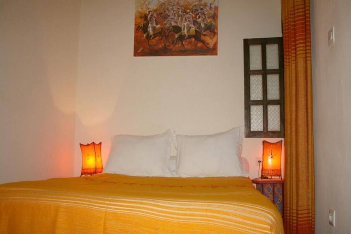 Uma cama com um cobertor listrado, duas luminárias de cabeceira, um quadro na parede e uma janela com cortinas.