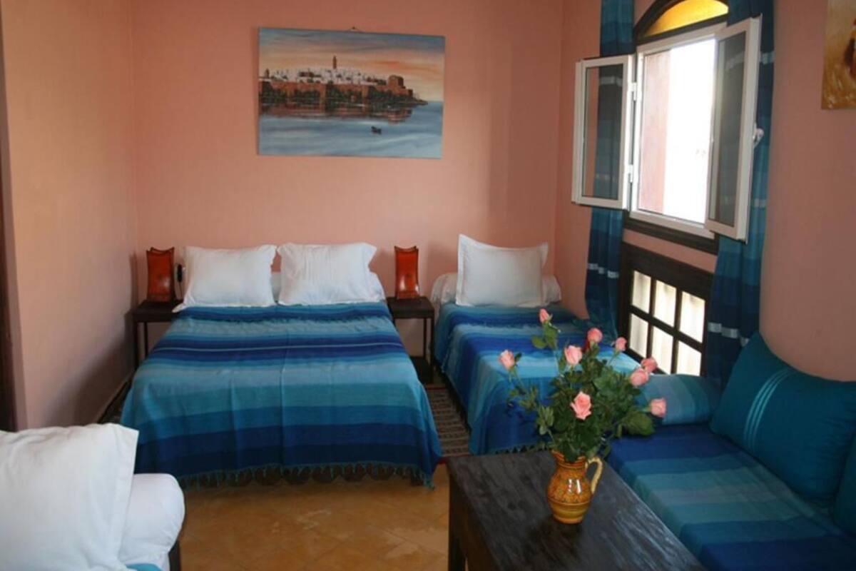 Quarto com duas camas, um sofá, uma mesa com um vaso de flores e um quadro na parede.