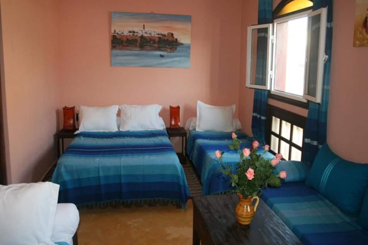 A room with two beds, a sofa, a table with a vase of flowers, and a painting on the wall.