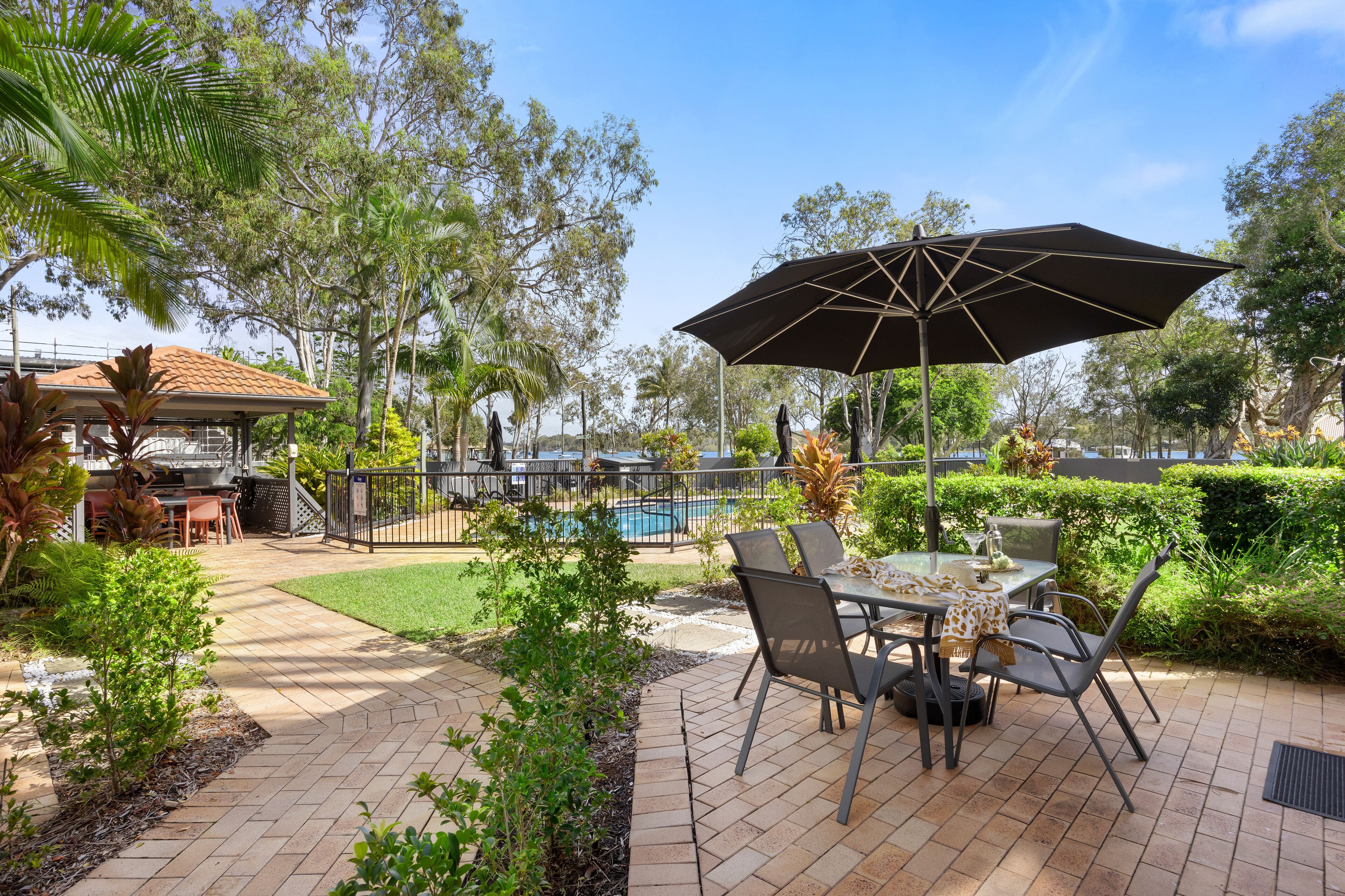 Eine Außenpatio-Terrasse mit Pool, Esstisch, Stühlen und einem großen Sonnenschirm.