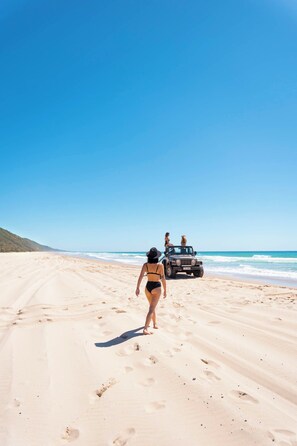A sandy beach with footprints leading to a vehicle. - Como Noosa (Noosaville)
