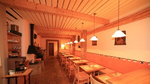 A long dining area with wooden tables and chairs, a brick wall, and hanging pendant lights.