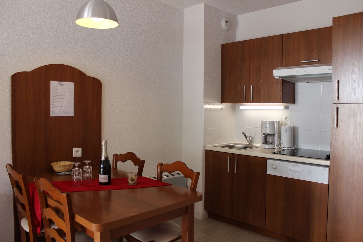 Une cuisine compacte avec des meubles en bois, une table à manger avec des chaises, une machine à café et un lave-vaisselle.