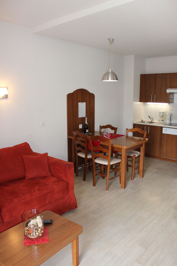 A compact living space with a dining area, kitchenette, and a red sofa.