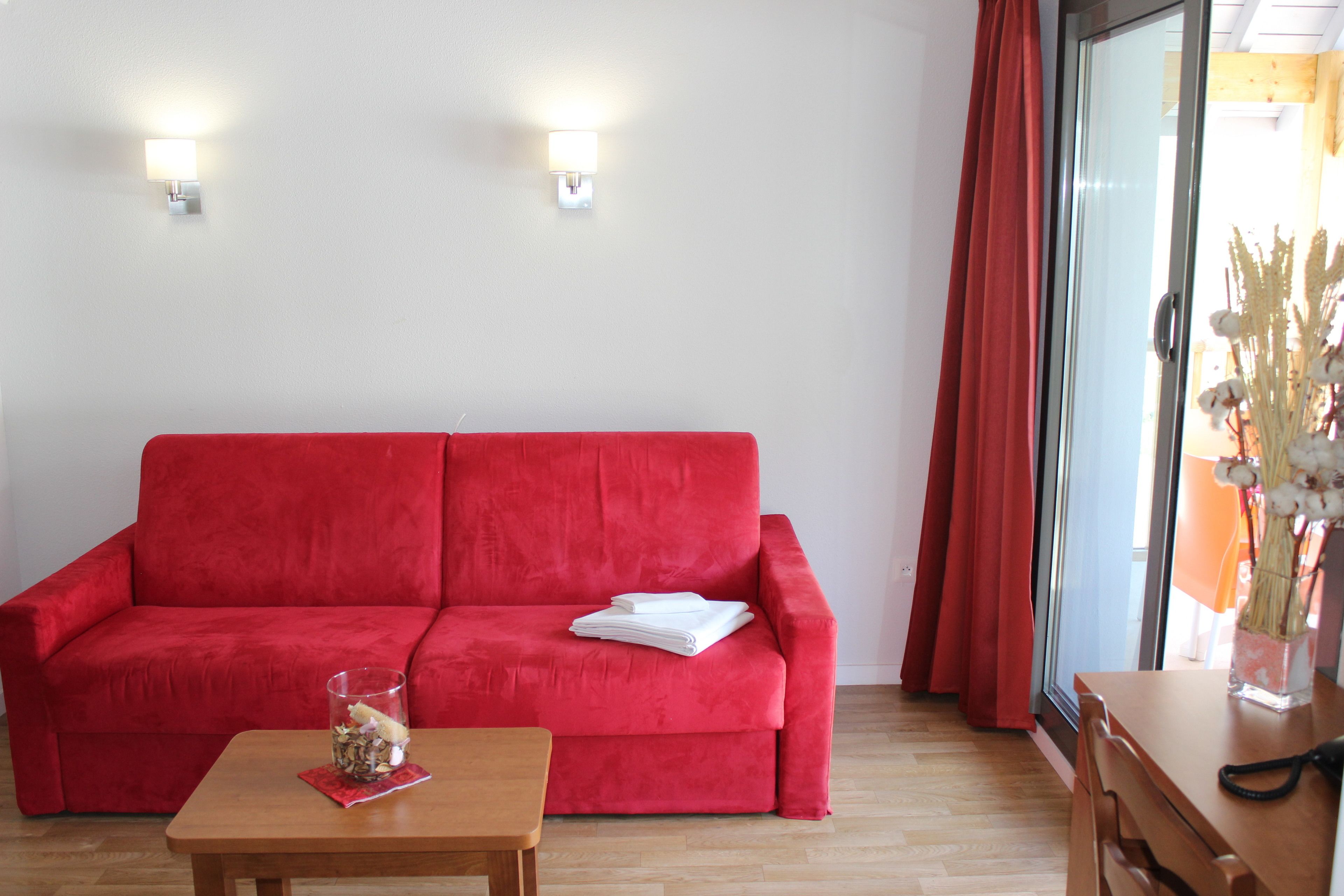 Un sofá rojo, una mesa de madera con un florero de vidrio y un escritorio de madera con un teléfono.