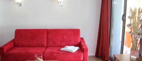 Un sofá rojo, una mesa de madera con un florero de vidrio y un escritorio de madera con un teléfono.