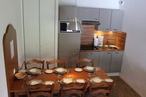 Ein Essbereich mit einem Holztisch, gedeckt für sechs Personen, umgeben von Stühlen. Eine Küche mit grauen Schränken und einer Holz Arbeitsplatte grenzt an den Essbereich.