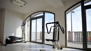 A gym with cardio machines and a rowing machine, large windows with a view of mountains, and a balcony with a railing. - Résidence Tourmalet (Bagnères-de-Bigorre)