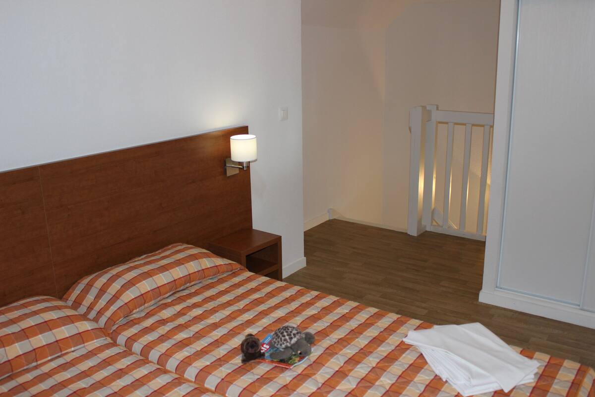 Ein ordentlich bezogenes Bett mit karierter Bettdecke, ein Nachttisch mit Lampe und Holzboden.