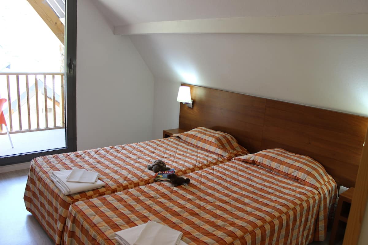 Ein Zimmer mit zwei Betten, jeweils mit kariertem Überwurf, einem Holzkopfende und einem Nachttisch mit Lampe.