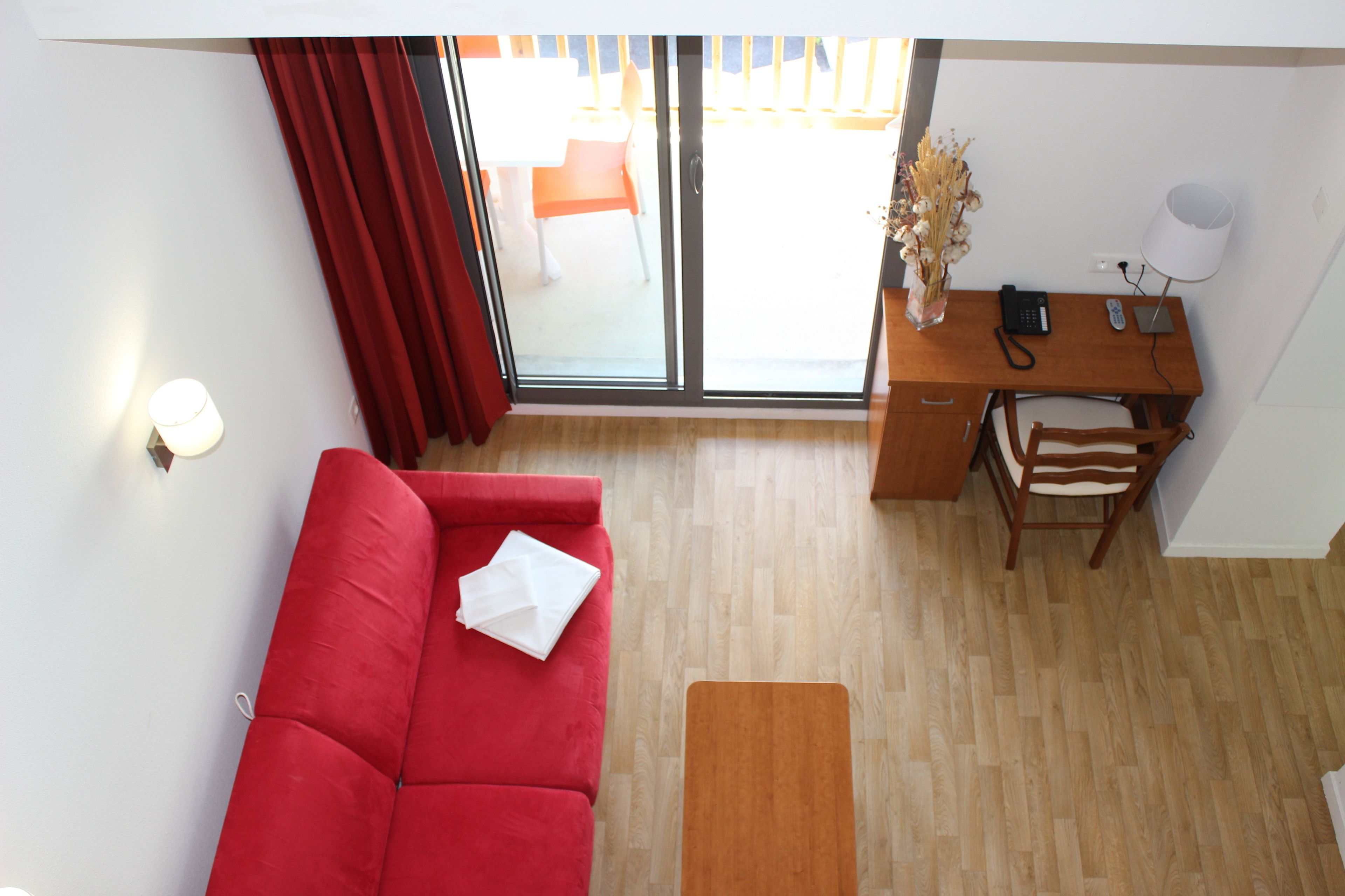 A modern living room with a red sofa, a wooden desk, and a view of the outdoor patio.