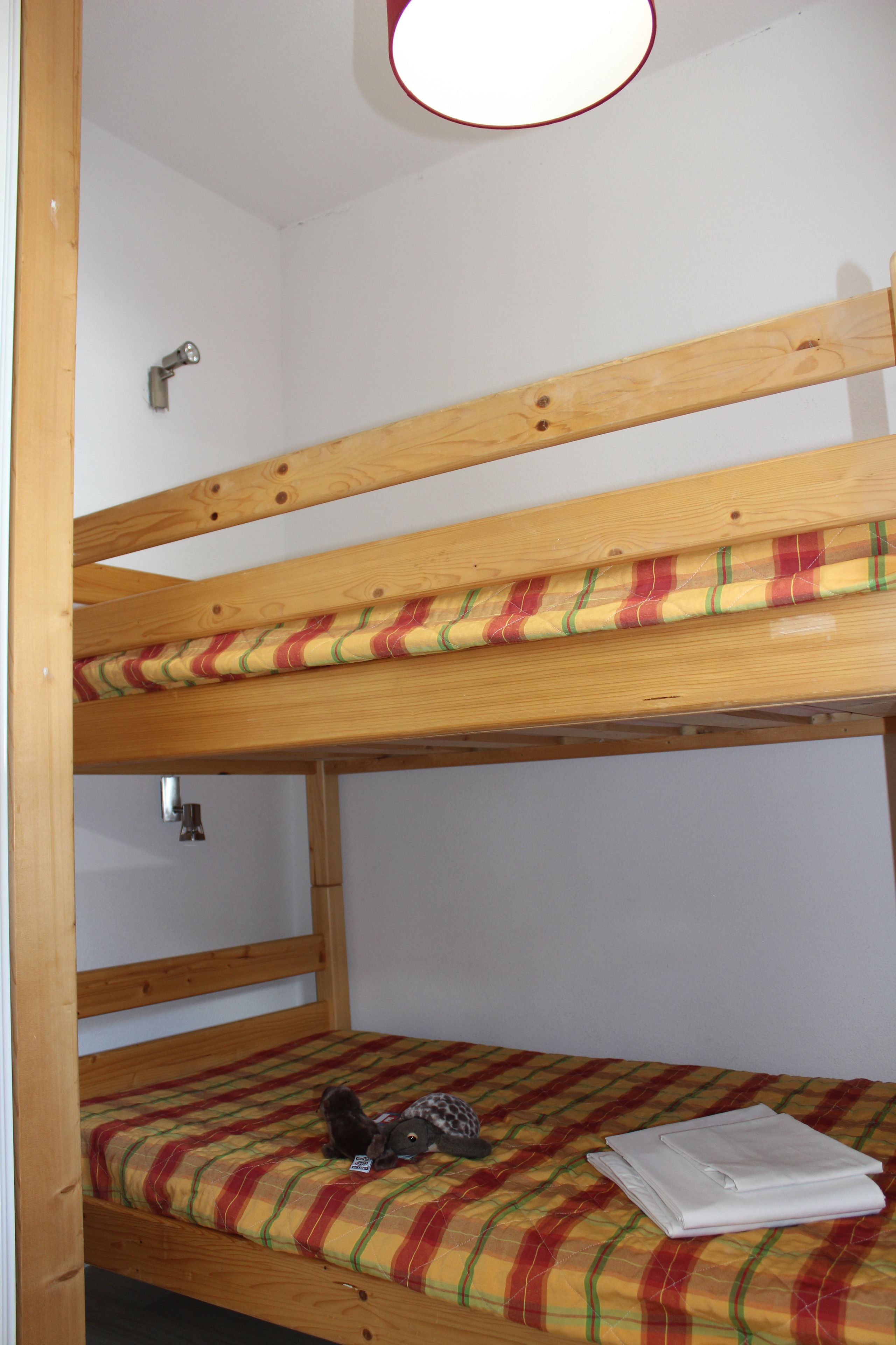 Un lit superposé avec une couverture à carreaux et une serviette blanche pliée sur le lit du bas.