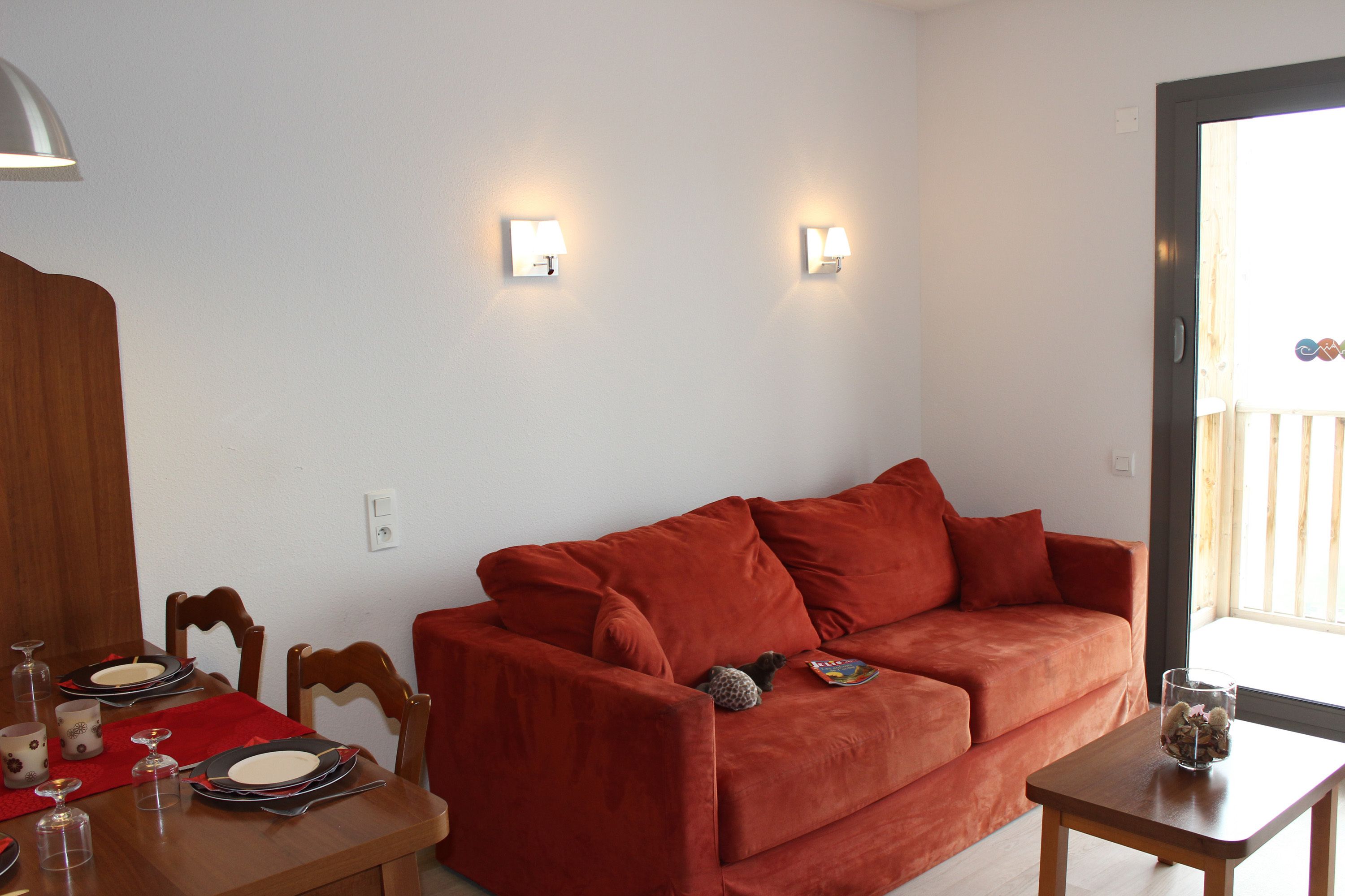 Una sala de estar con un sofá rojo, una mesa de centro de madera y un comedor con mantel y platos rojos.