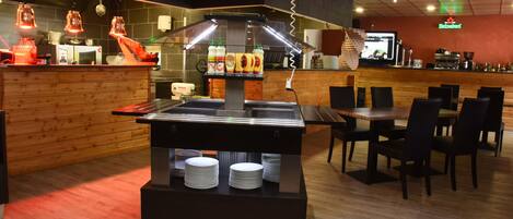 A restaurant with a buffet counter, wooden tables, and chairs.