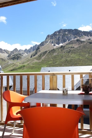 A wooden deck with a table and orange chairs, overlooking a mountainous landscape.