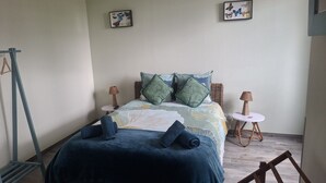 Un dormitorio con una cama, dos mesitas de noche, un sillón colgante y dos cuadros en la pared.