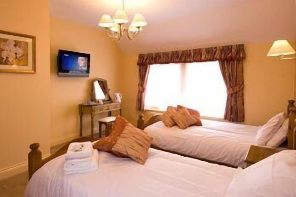A hotel room with two beds, a desk, a television, and a window with curtains.
