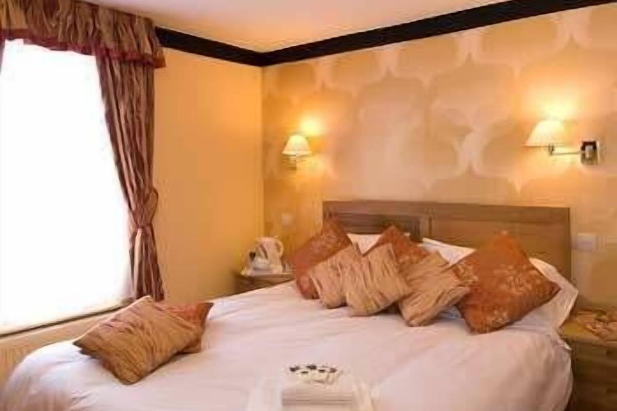 A hotel room with a neatly made bed, a bedside table with a lamp, and a window with curtains.