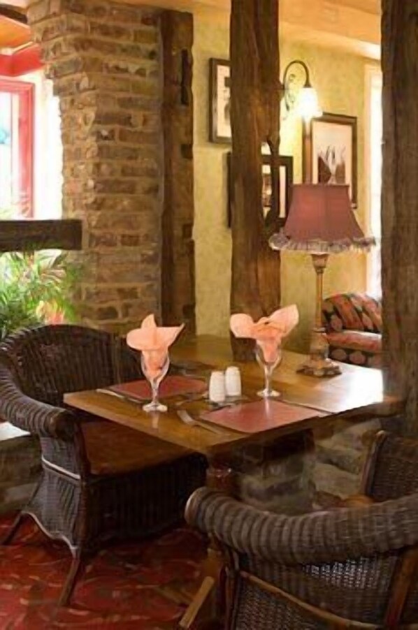 Un comedor con sillas de mimbre, una mesa de madera y una pared de piedra.