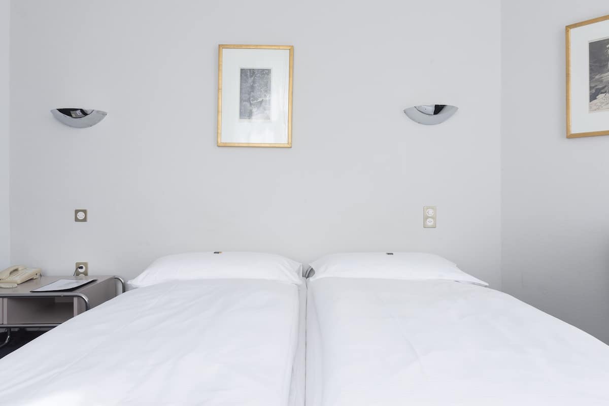 A hotel room with two beds, a bedside table with a phone, and framed pictures on the wall.