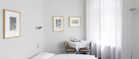 A hotel room with a bed, a small table with chairs, and framed pictures on the wall.