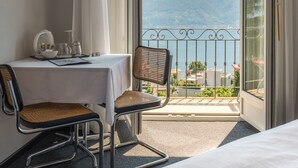 A hotel room with a bed, a table with a chair, a view of mountains through a balcony. - Monte Verità (Ascona)