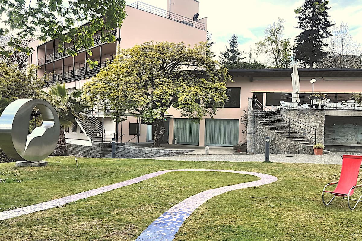 A modern building with a staircase leading to a rooftop terrace, surrounded by greenery and a red chair.