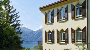 A building with multiple windows, a balcony, and a view of a lake and mountains. - Monte Verità (Ascona)