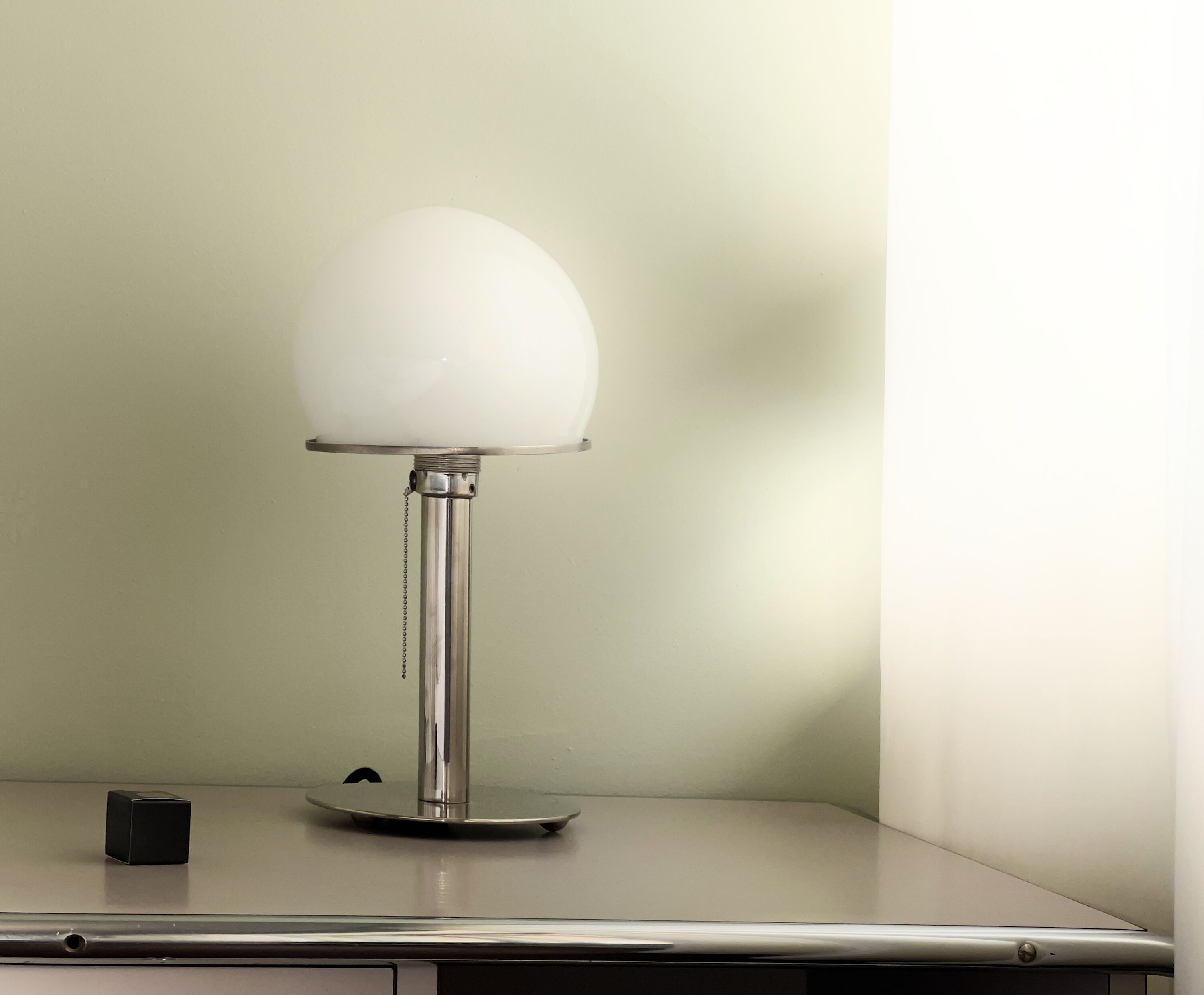 A table with a modern table lamp, a small black object, and a metallic base.