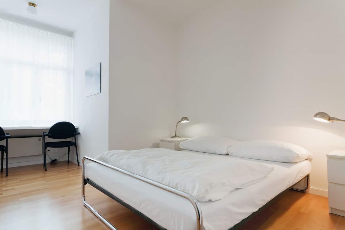 A minimalist bedroom with a bed, bedside tables, a desk, and a chair.
