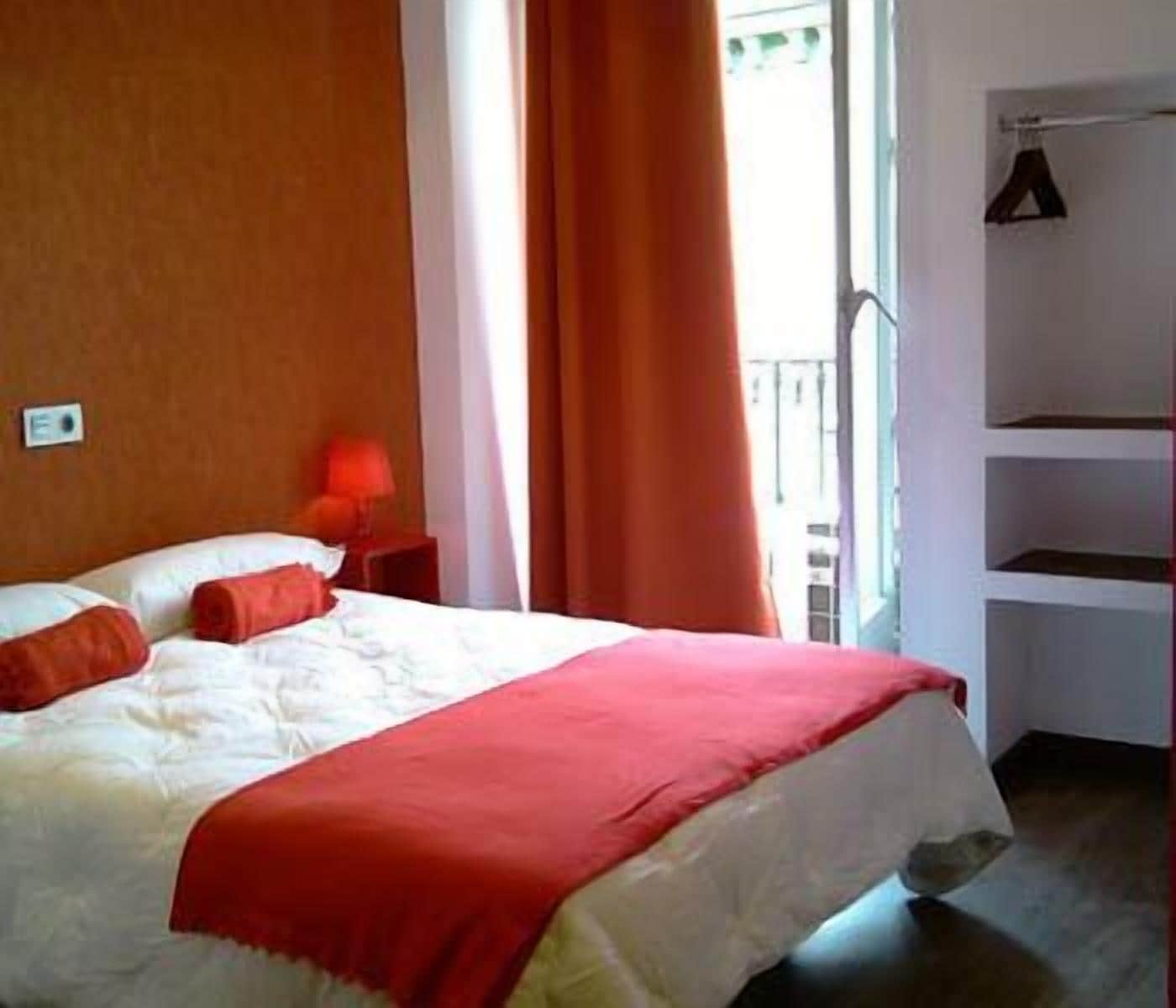 A hotel room with a bed, a nightstand, a red lamp, and a window with curtains.