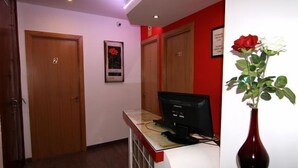 A reception desk with a computer, a vase with a rose, and two wooden doors. - Hostal Abril (Madrid)