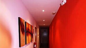 A hallway with a red wall on one side and a pink wall on the other, featuring artwork and a fire extinguisher. - Hostal Abril (Madrid)