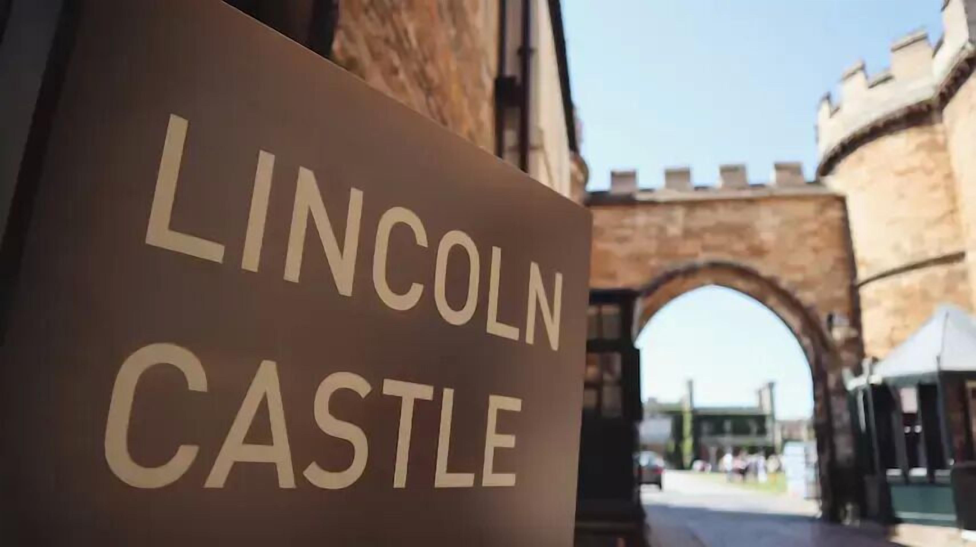 A sign for Lincoln Castle with an arched gateway in the background.