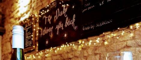 A bottle of Macon-Vill wine, a lit candle, and two glasses of white wine on a table with a stone wall and a menu in the background.