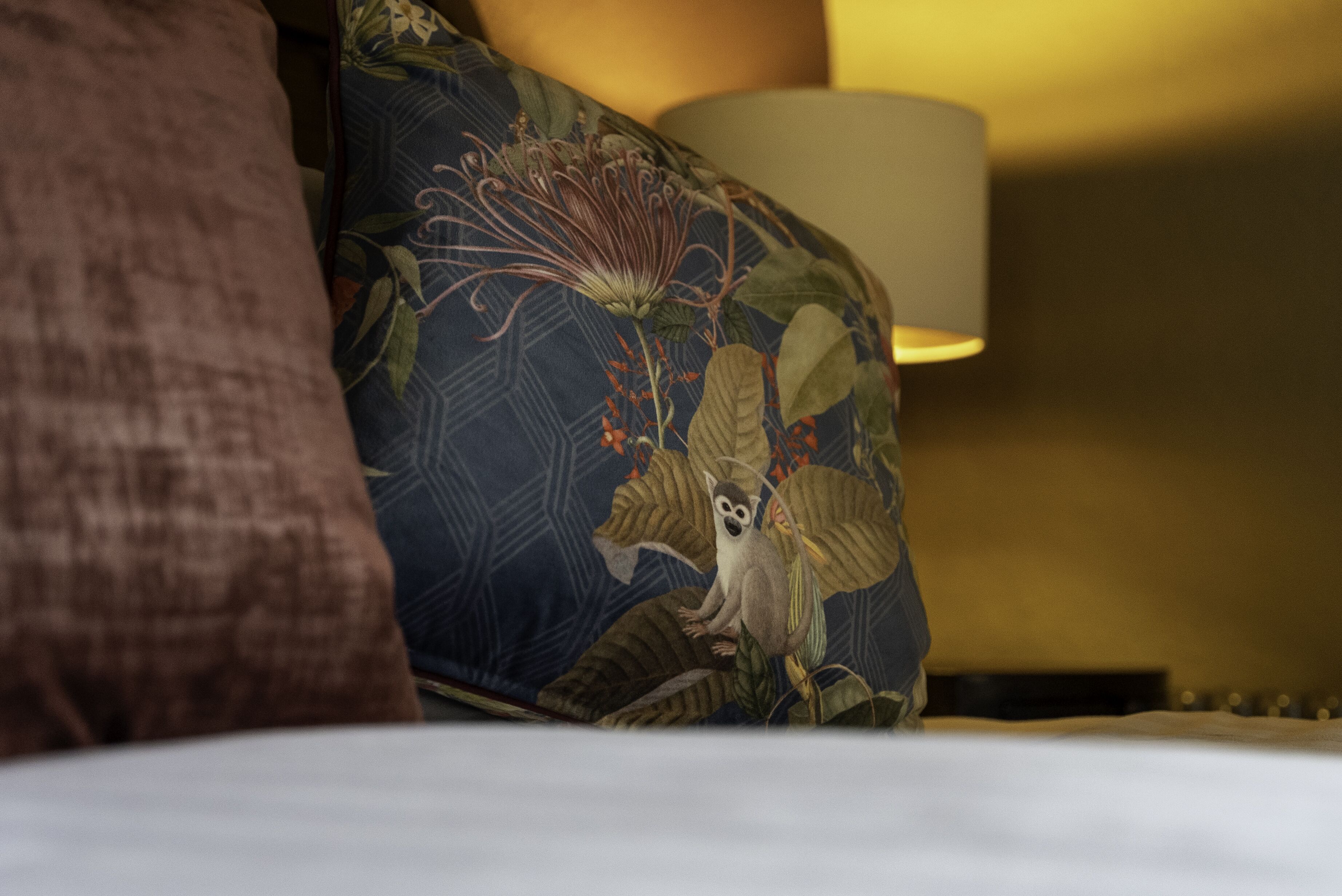 A bed with a blue pillow featuring a lemur design, a brown pillow, and a lamp with a beige shade.