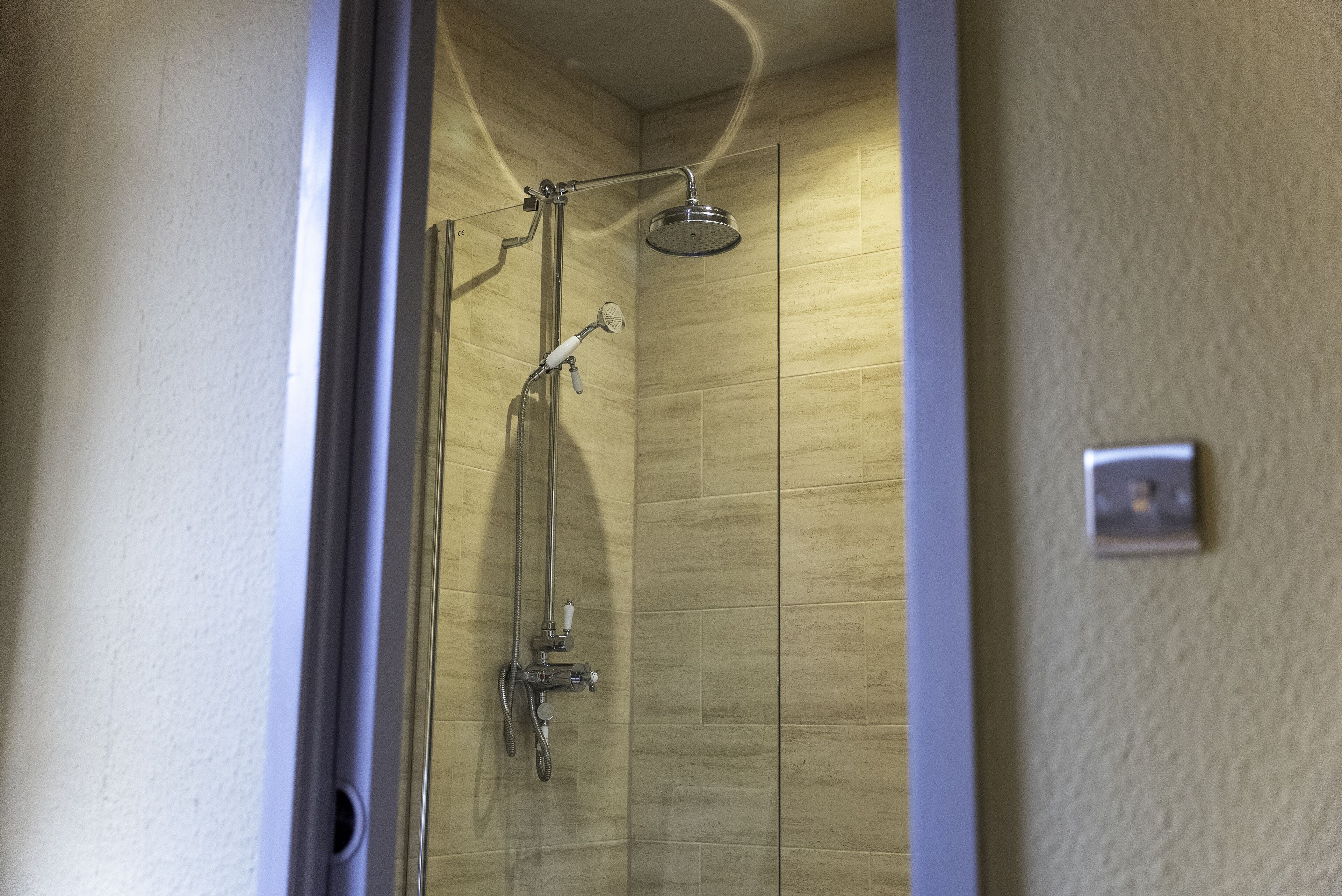 A shower with a handheld showerhead and a wall-mounted faucet.