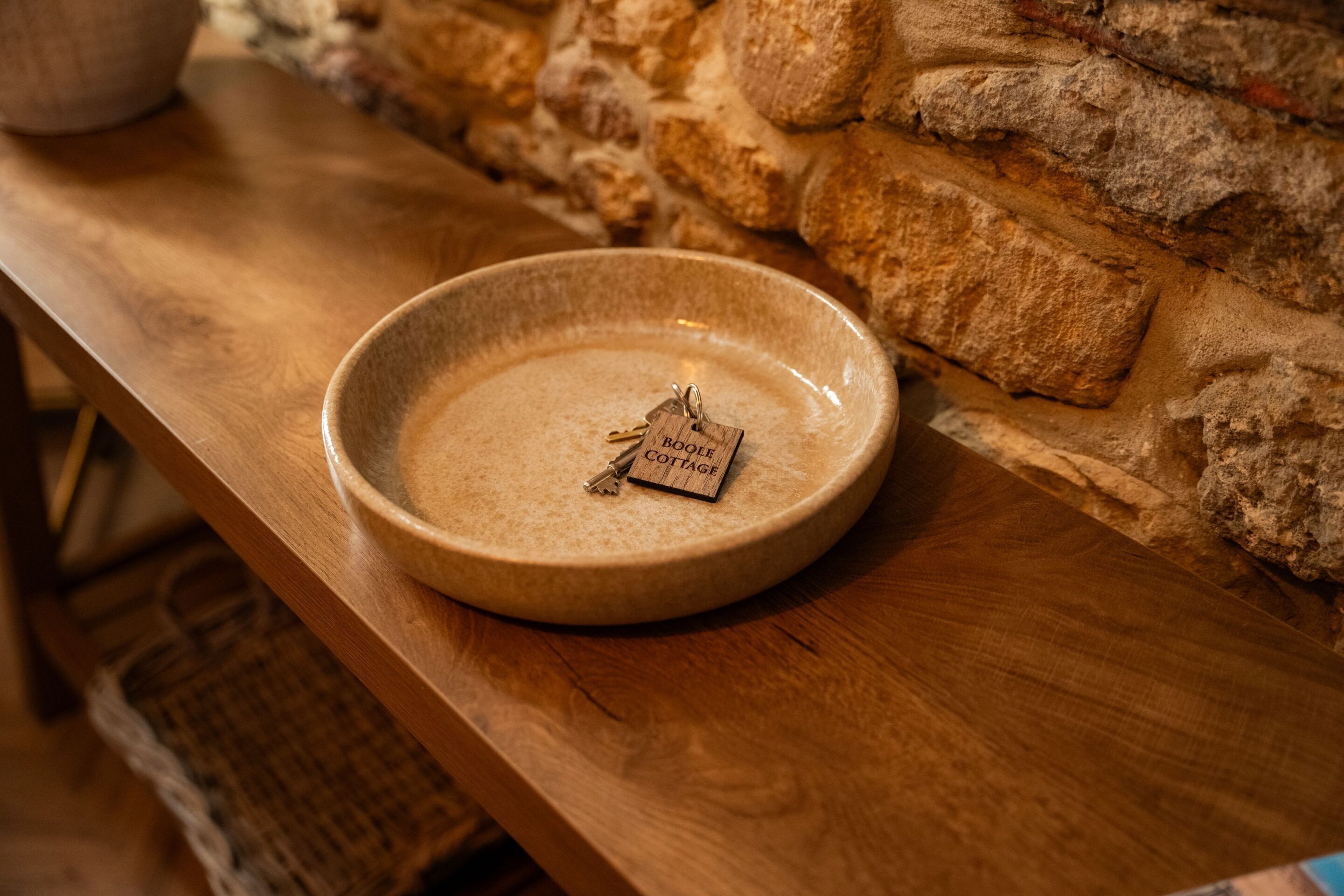 A wooden table with a ceramic bowl containing a key and a tag labeled "Boodle Cottage."